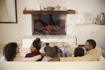 Family Sitting On Sofa In Lounge Next To Open Fire