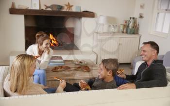 Family Sitting On Sofa In Lounge Next To Open Fire Eating Pizza