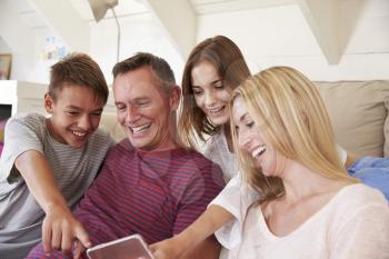 Family With Teenage Children Sitting On Sofa Looking At Mobile Phone At Home