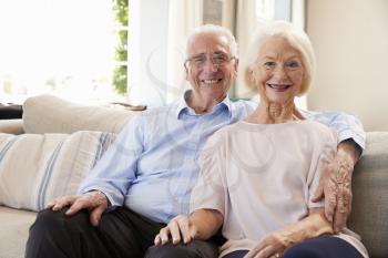 Portrait Of Smiling Senior Couple Sitting On Sofa At Home