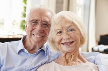 Portrait Of Smiling Senior Couple Sitting On Sofa At Home