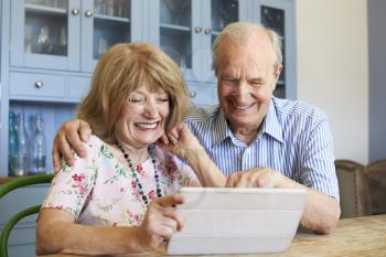 Senior Couple Sit At Home Using Digital Tablet Together