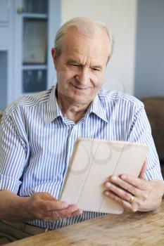 Senior Man Sitting At Home Using Digital Tablet At Table