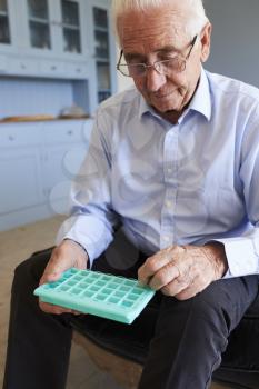 Senior Man At Home Using Pill Organiser For Medication