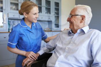 Nurse Talking With Senior Man Sitting In Chair On Home Visit
