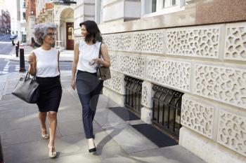 Two women walking in the street talking, full length