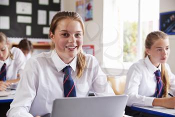 Portrait Of Female Pupil In Uniform Using Laptop In Classroom
