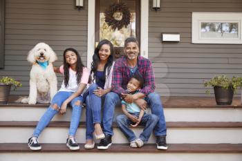 Family With Children And Pet Dog Sit On Steps Of Home