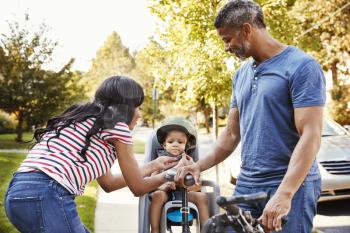Parents Putting Daughter Into Child Seat For Bike Ride