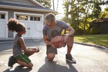 Father Teaching Son How To Play Basketball On Driveway At Home