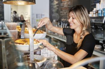 Waitress Behind Counter In Coffee Shop Cutting Slice Of Cake