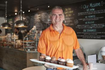 Portrait Of Male Owner With Tray Of Muffins In Coffee Shop