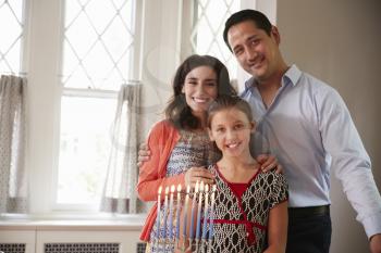 Jewish parents and daughter smiling, lit candles on menorah