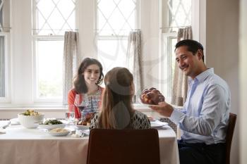 Jewish man holding challah bread at Shabbat meal with family