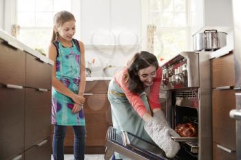 Mother taking bread out of the oven while daughter watches