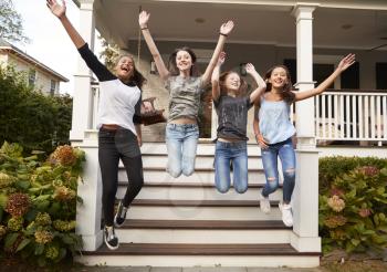 Four young teen girls jumping from front steps of a house