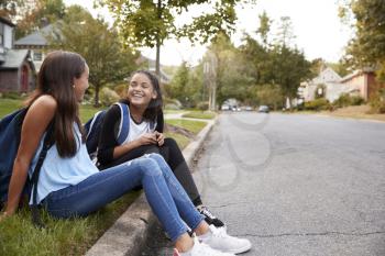 Two teen girlfriends sit talking at the roadside