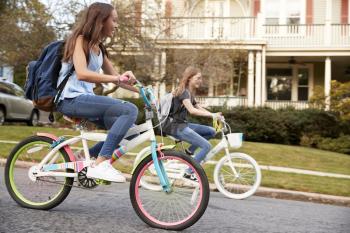Two teen girls riding bikes in street, side view close up
