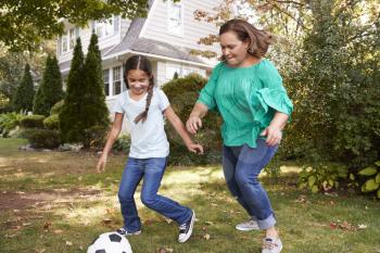Grandmother Playing Soccer In Garden With Granddaughter