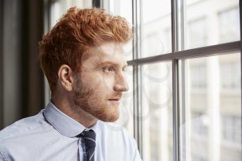Young red haired bearded businessman looking out of window