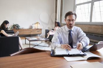 Businessman working at desk, female colleagues in background