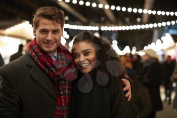 Portrait Of Couple Enjoying Christmas Market At Night