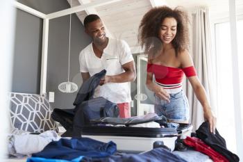 Couple In Bedroom Packing Suitcase For Vacation