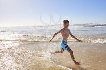 Boy On Summer Vacation Running Through Waves