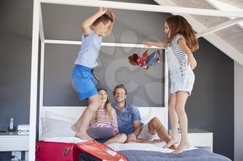 Excited Children Jump On Bed As Parents Pack For Vacation