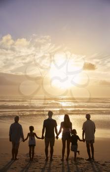 Rear View Of Multi Generation Family Silhouetted On Beach
