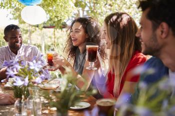 Young adult friends socialising at a table in a garden