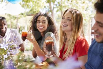 Young adult friends socialising at a table in a garden