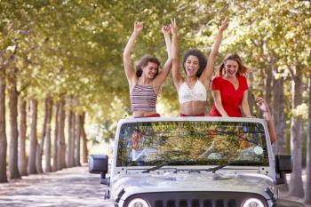 Girlfriends standing in an open top car with arms in the air