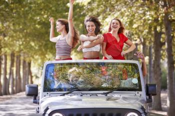 Girlfriends standing in an open top car with arms in the air