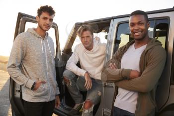 Three male friends on road trip looking at camera from jeep