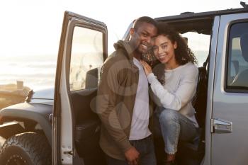 Young mixed race couple on a road trip embracing by car