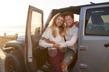 Young white couple on a road trip embracing by their car