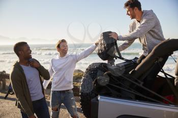 Three young adult male friends unloading backpacks from jeep