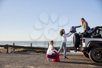 Three young adult girlfriends unloading backpacks from a car