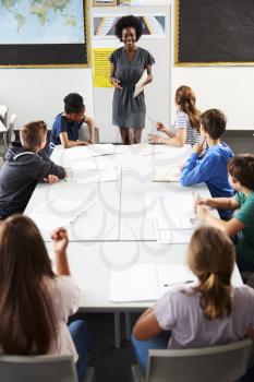 Female High School Tutor Standing By Table With Students Teaching Lesson