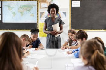 Portrait Of Female High School Teacher Standing By Table With Students In Lesson