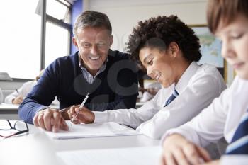 High School Tutor Giving Male Student Wearing Uniform One To One Tuition At Desk