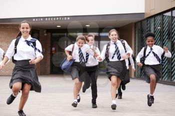 Group Of High School Students Wearing Uniform Running Out Of School Buildings Towards Camera At The End Of Class