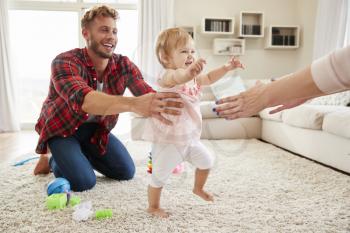 Toddler girl walking from dad to mums arms in sitting room