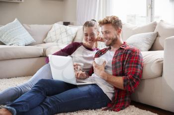 Young white couple sitting on the floor at home using laptop