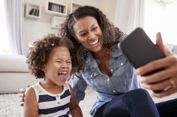 Young mother and toddler daughter taking selfie at home