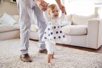 Father helping daughter learn to walk in the sitting room