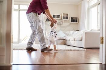 Father helping daughter learn to walk at home, side view