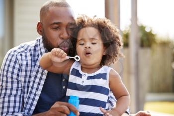 Young black father and daughter blowing bubbles outside