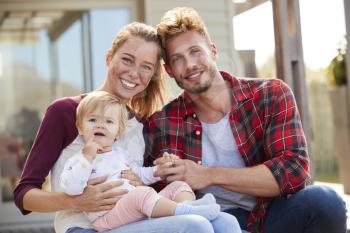Young white family sitting and smiling at camera outside